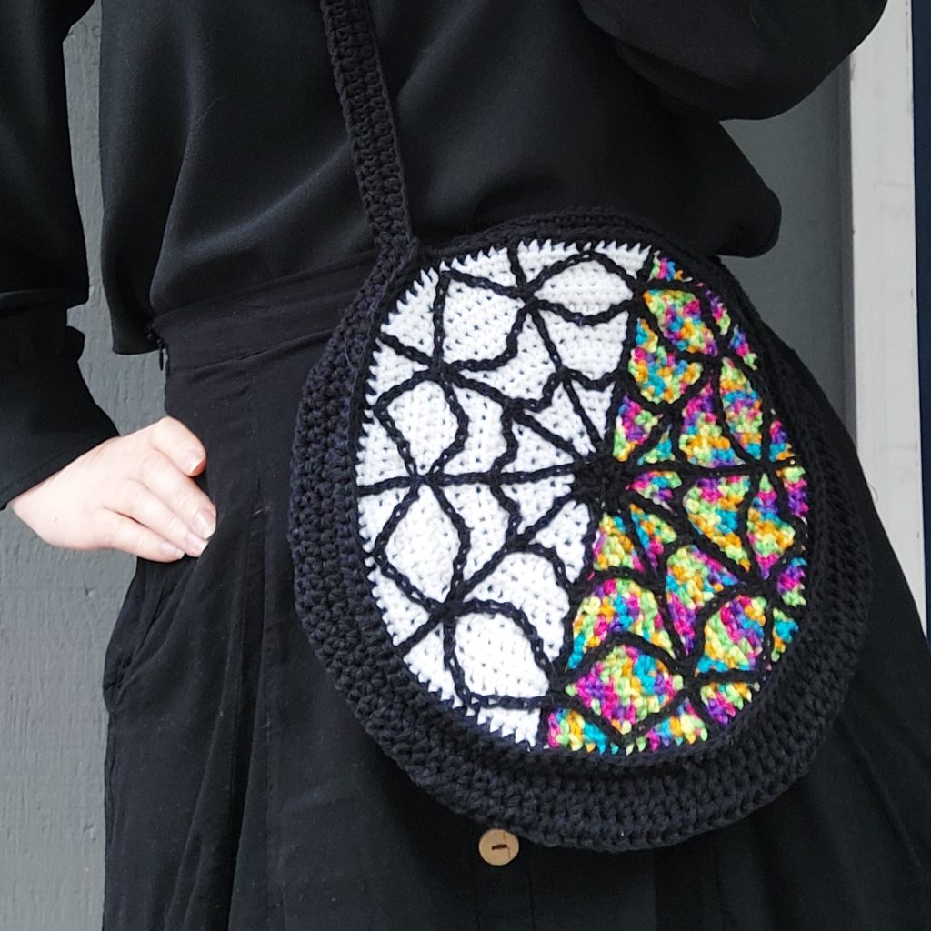 Wednesday Crochet Pattern inspired by the Netflix show: a crochet round bag that's half rainbow, and half white with black overlay.